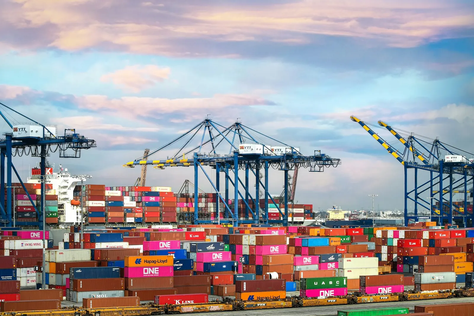 Colourful shipping containers stacked in rows beside a quayside crane.