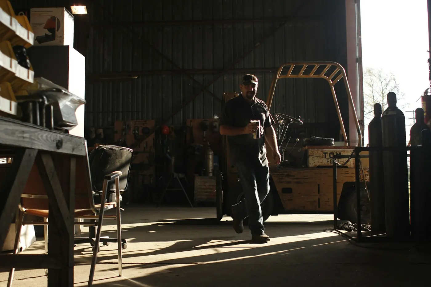 Warehouse operator walking past a forklift in a dimly lit storage hall.